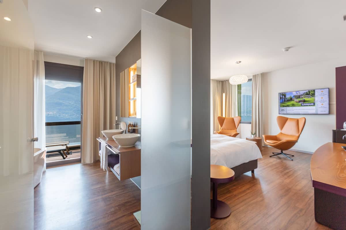 Habitación de hotel con un ventanal grande, una cama, un escritorio, una silla y un baño.