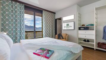 A hotel room with a bed, a view of mountains, a wardrobe, and a framed sign on the wall.