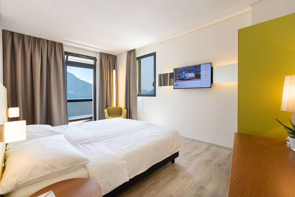 Habitación de hotel con una cama grande, una silla, un escritorio y un televisor en la pared.