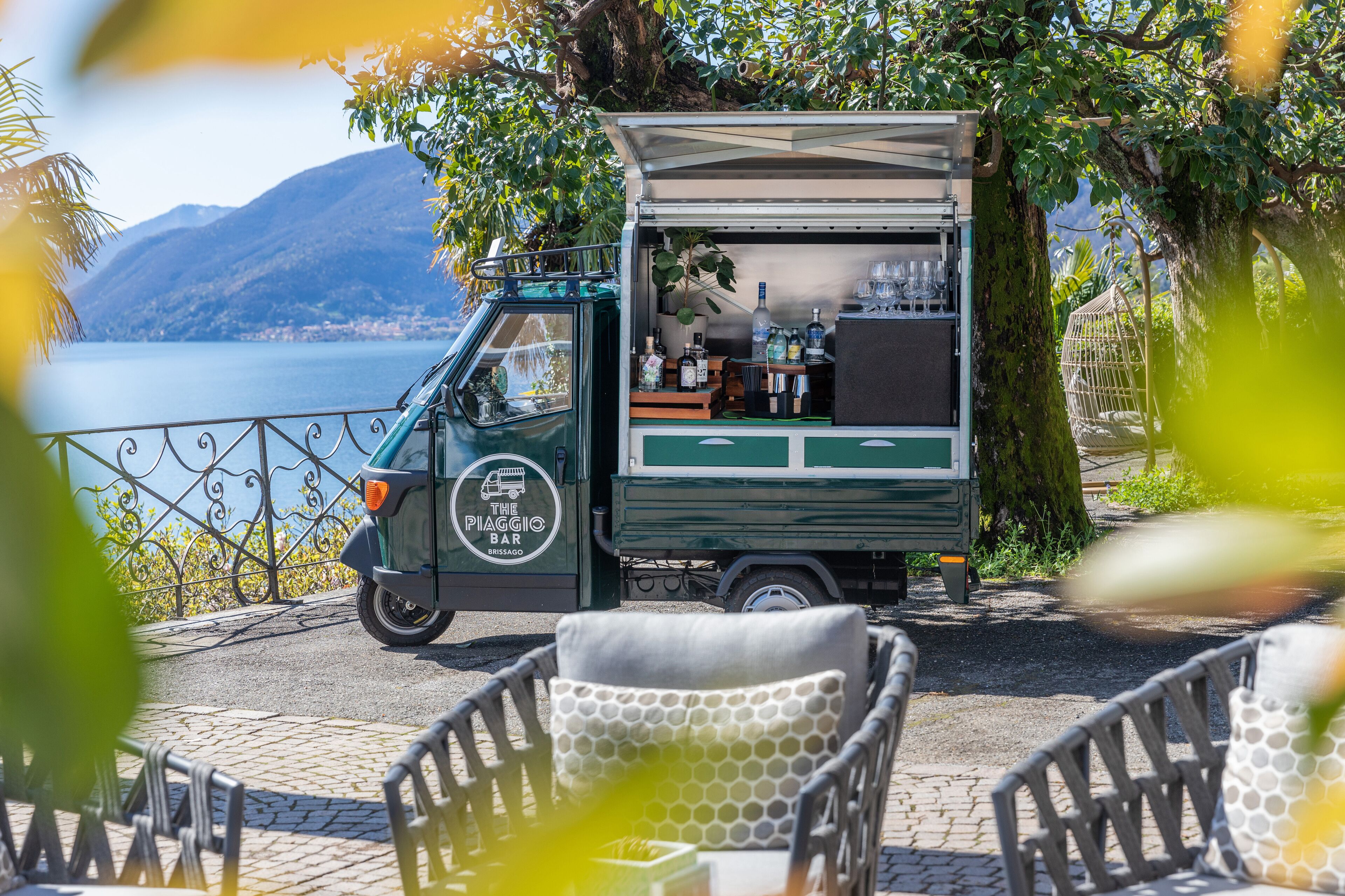 A food truck with a menu and drinks, parked near a scenic lake with chairs in the foreground.