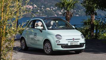 A light blue car with "BRESCINO" branding parked on a paved area with a scenic coastal background.
