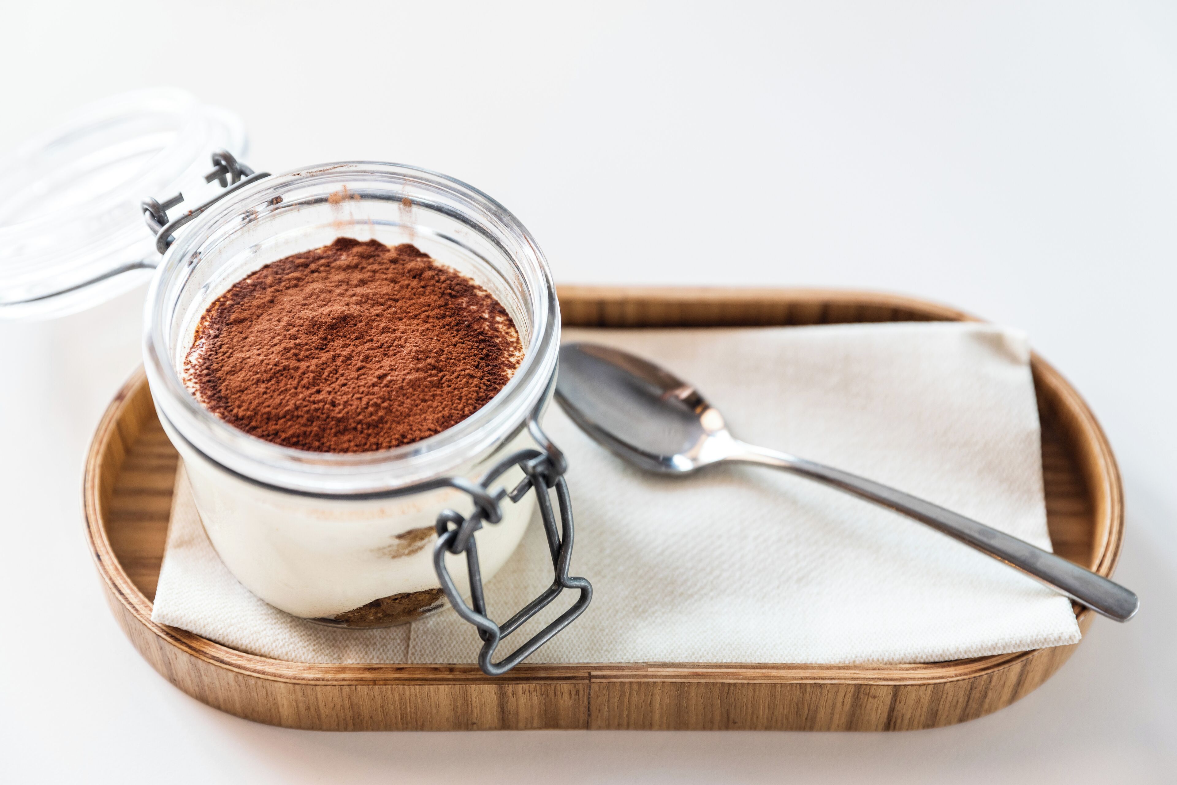 A jar of dessert with a spoon on a wooden tray.