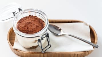 A jar of dessert with a spoon on a wooden tray.