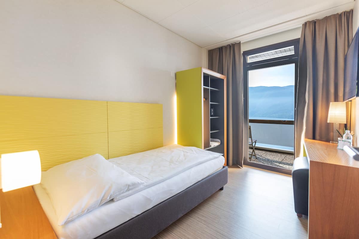 Habitación de hotel con cama, escritorio, armario y vistas al exterior.