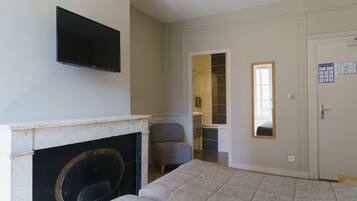 A bedroom with a fireplace, a television mounted on the wall, a bed, a chair, and a door leading to a bathroom.