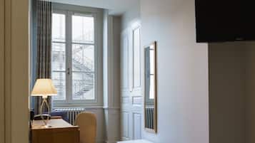 Una camera d'albergo con un letto, una scrivania con una lampada, una sedia, una televisione e una finestra con tende.
