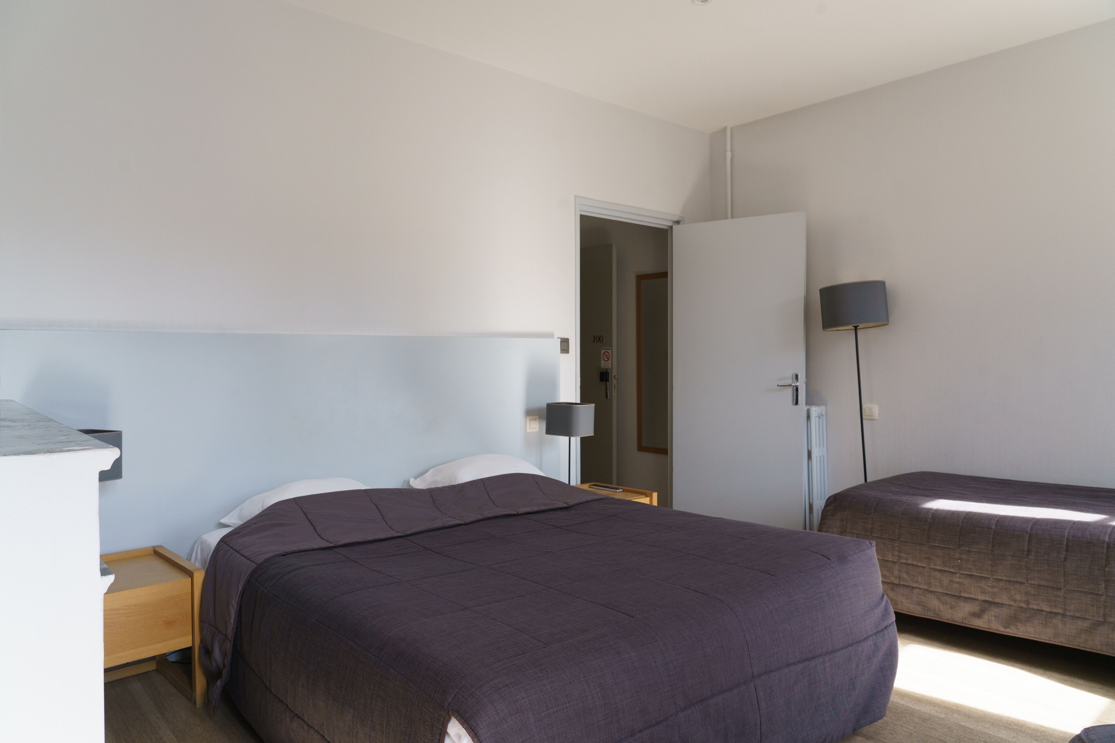 A bedroom with a large bed, a smaller bed, a nightstand, a lamp, and a door leading to another room.