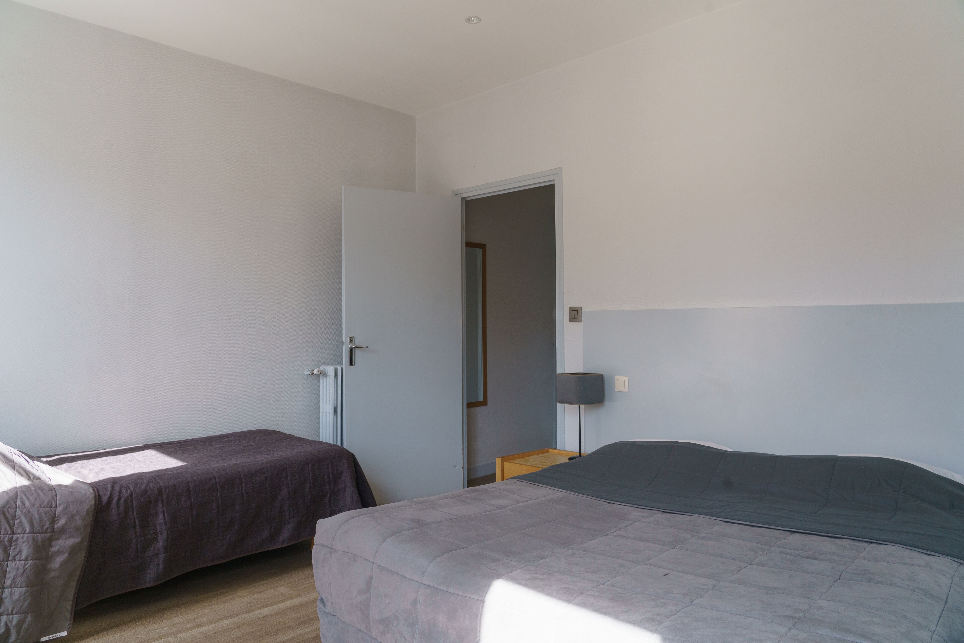 A bedroom with two beds, a door, a nightstand, and a lamp.