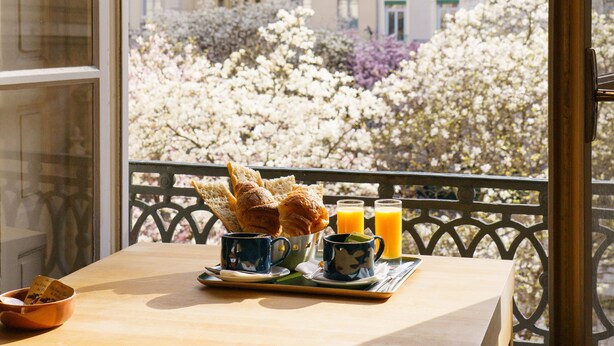 A balcony with a wooden table, two cups, a plate with pastries, and a glass of orange juice. - Hotel du Theatre (Lyon)