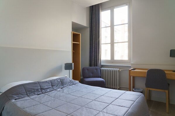 A hotel room with a bed, a desk, a chair, a wardrobe, and a window. - Hotel du Theatre (Lyon)