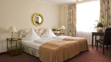 A hotel room with a large bed, two bedside tables with lamps, a mirror, a desk with a chair, and a window with curtains.