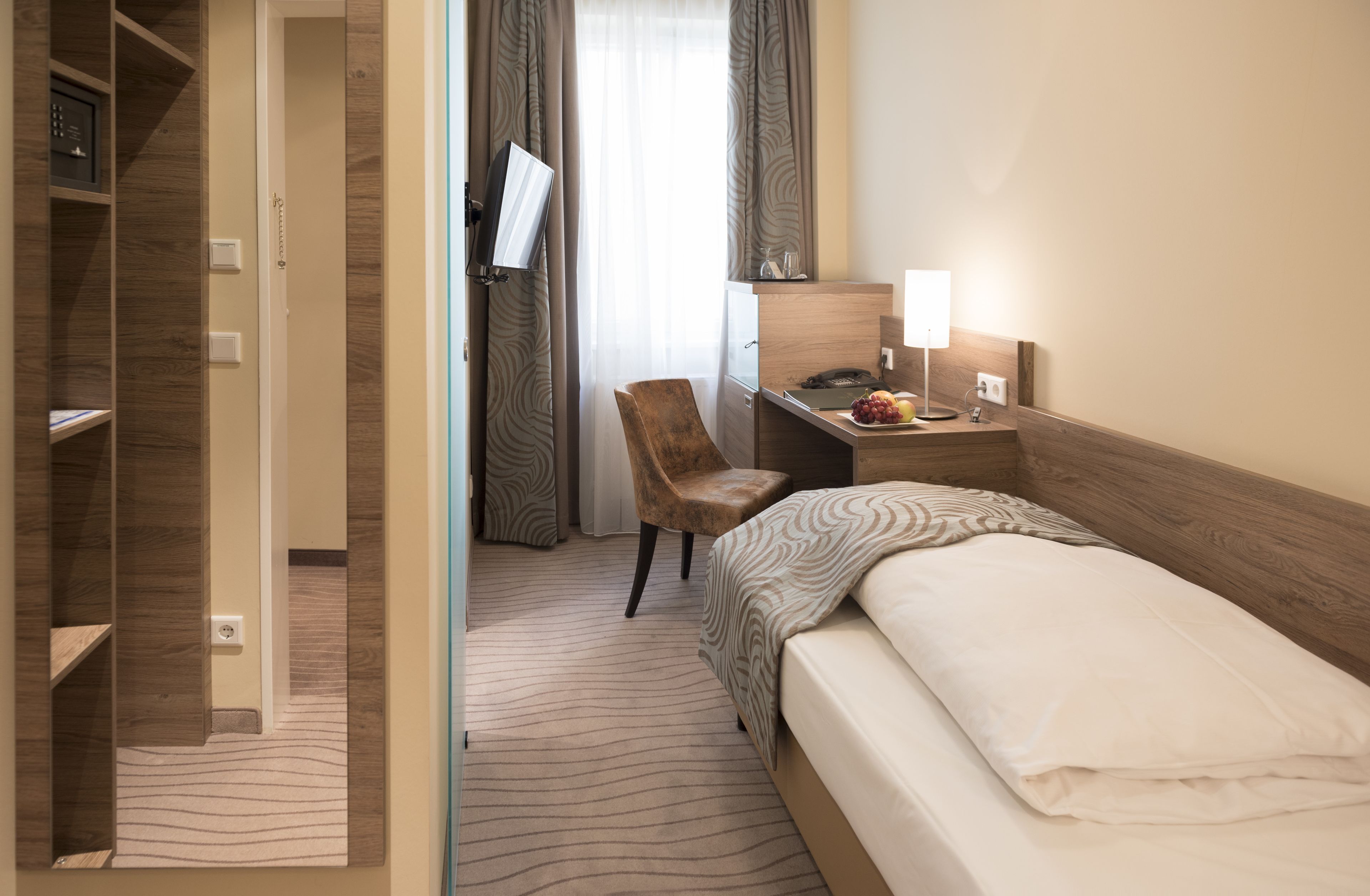 Ett hotellrum med en säng, ett skrivbord med en lampa, en stol, en tv och en garderob.