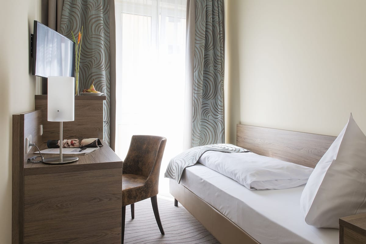 Habitación de hotel con cama, escritorio, computadora, silla y televisor en la pared.