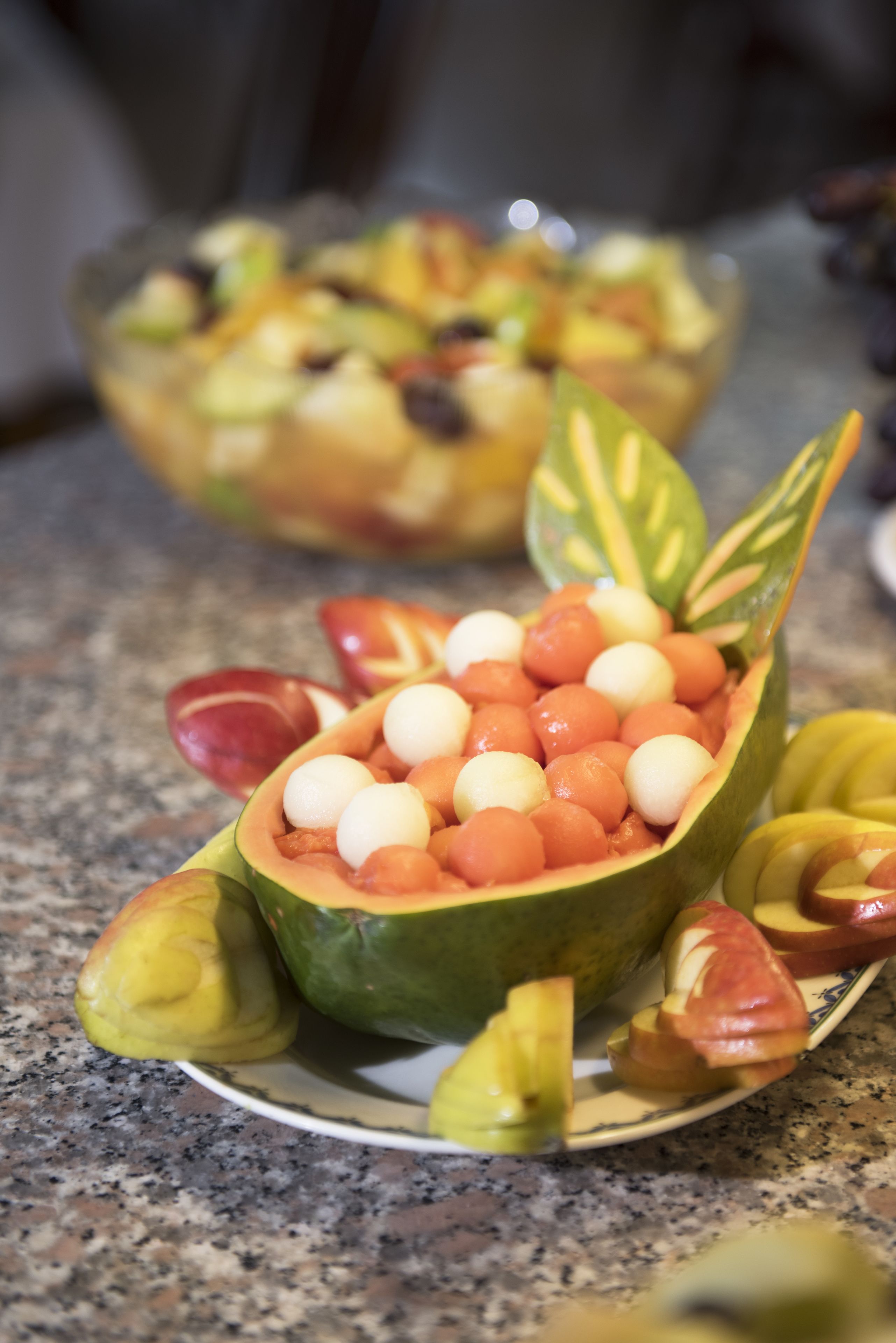 Une salade de fruits servie dans une demi-papaye évidée, posée sur un plan de travail en granit.