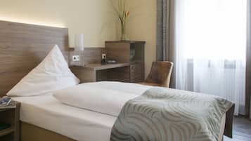 Una habitación de hotel con cama, escritorio, silla, mesita de noche y un jarrón con flores.