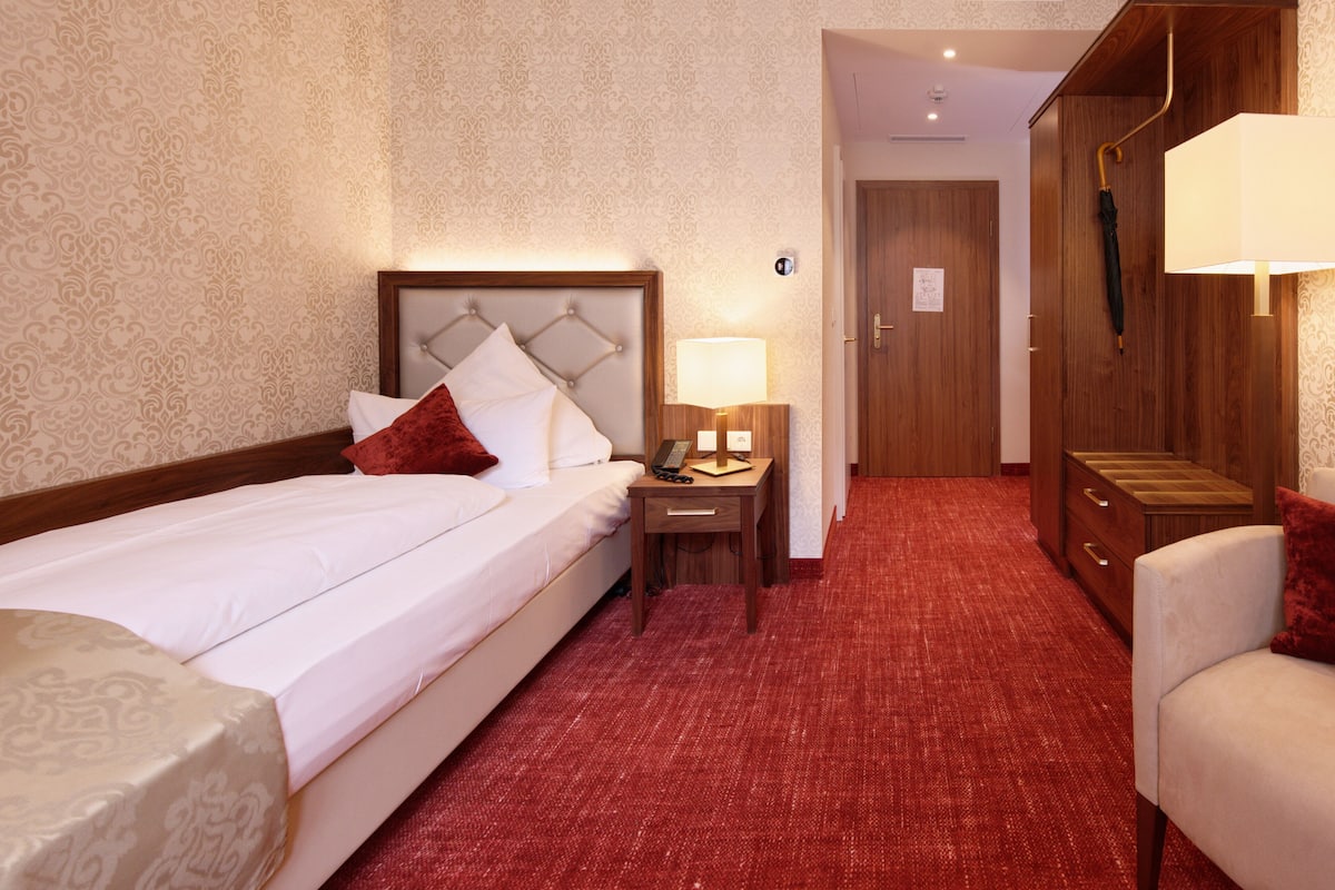 Una habitación de hotel con cama, mesita de noche, escritorio, armario y alfombra roja.