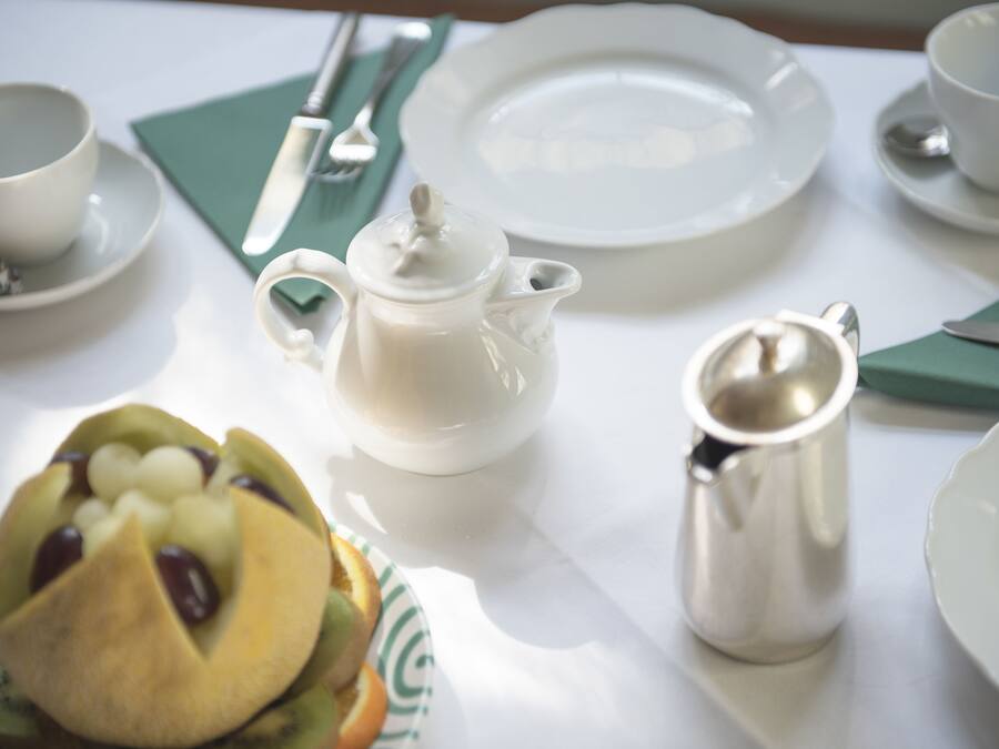 A table set with white plates, a teapot, a cup, a silver pitcher, and a fruit arrangement.