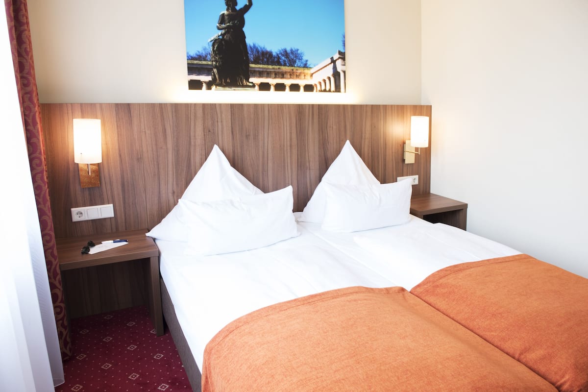 Habitación de hotel con una cama grande, dos mesitas de noche y una lámpara fijada a la pared.