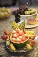 Un frutero con una disposición decorativa de frutas y un plato con fruta cortada.