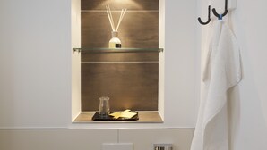 A bathroom with a glass shelf holding a bottle and a glass, and a towel hanging on a hook. - Hotel Schlicker (Munich)