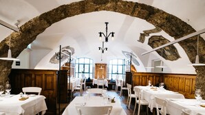 Un restaurante con mesas y sillas blancas, un arco de piedra y una araña.