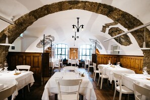 Un restaurante con mesas y sillas blancas, un arco de piedra y una araña.