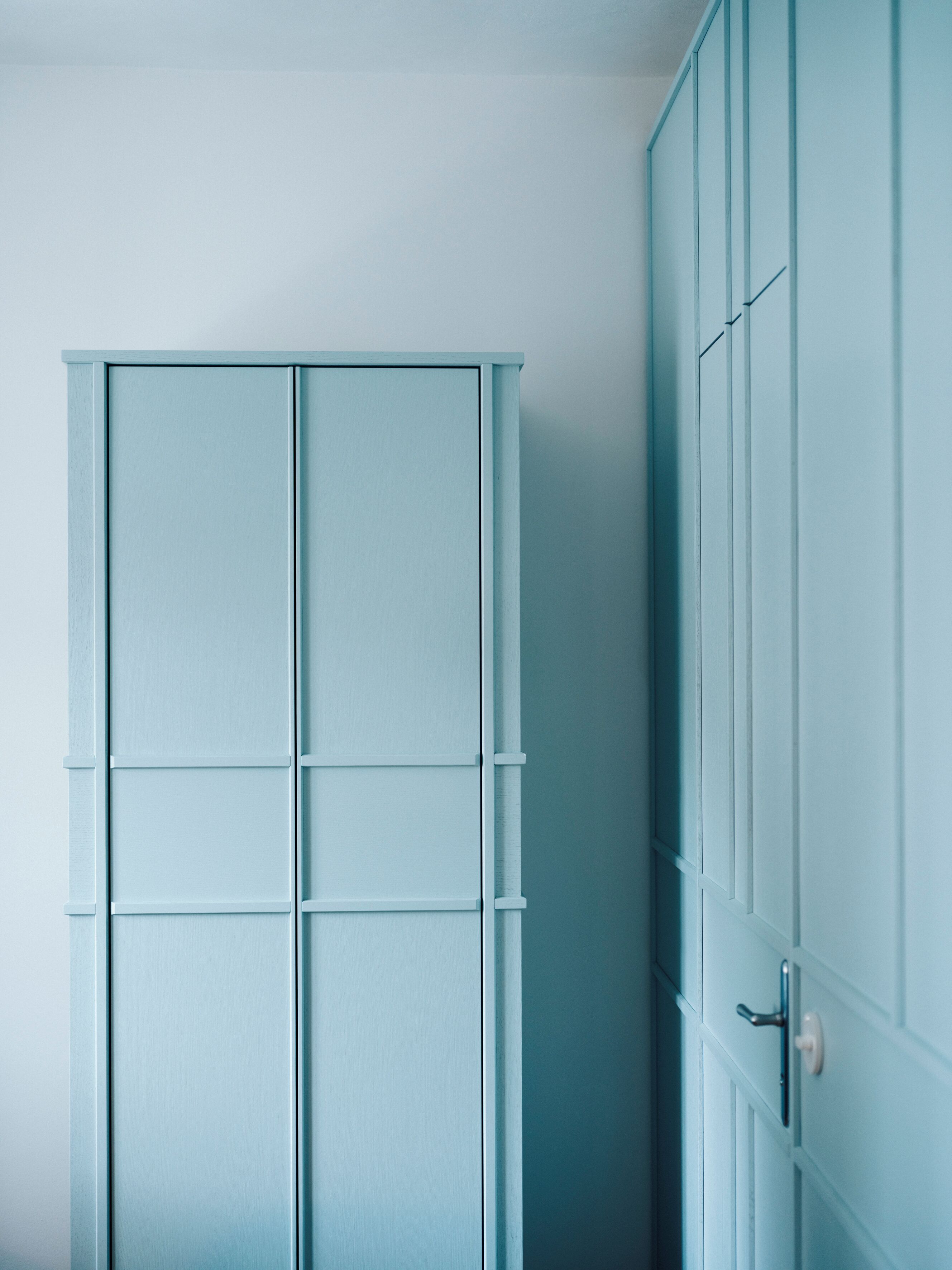 A room with a light blue wardrobe, a white door, and a white wall.