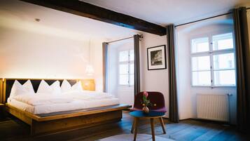 A bedroom with a wooden bed, a chair with a vase, and large windows.