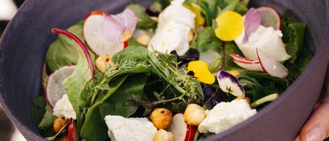 A bowl of salad with various greens, fruits, and nuts.