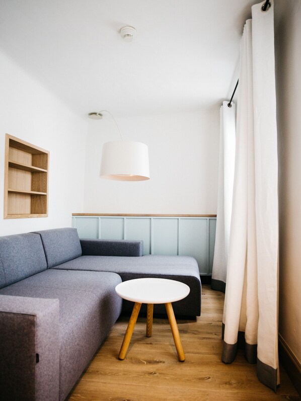 A modern, minimalist room with a grey sofa, a small round table, and a pendant light. - Arthotel Blaue Gans (Salzburg)
