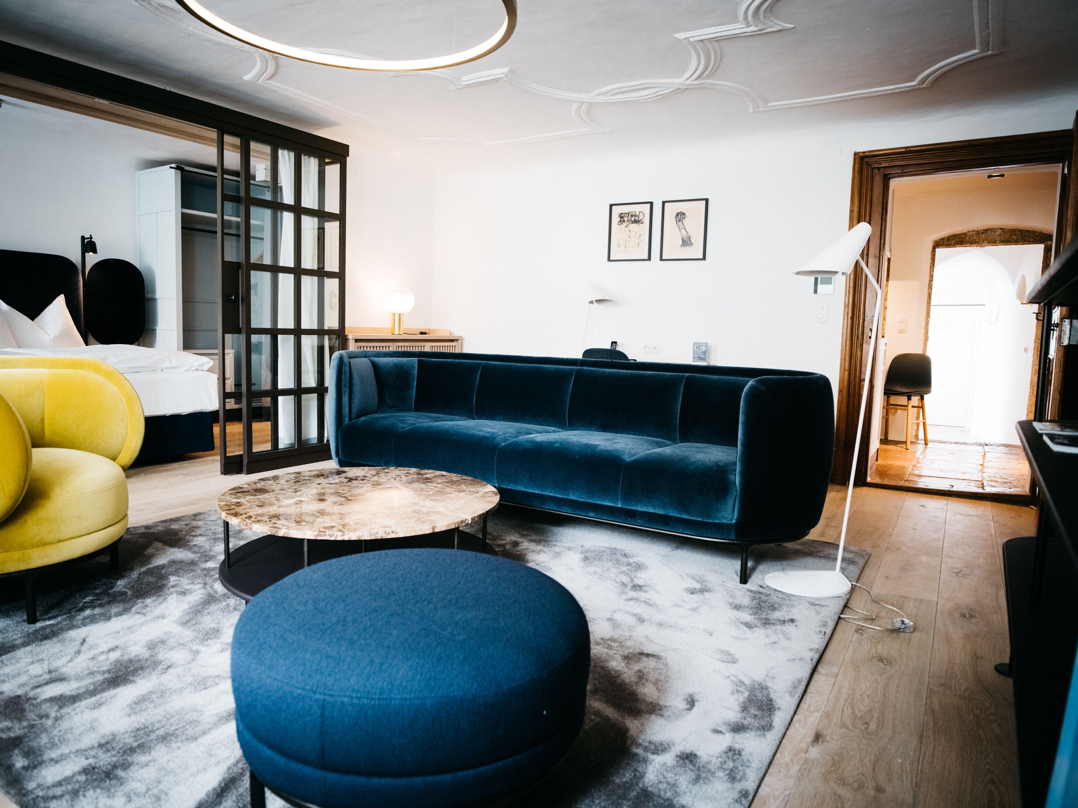 Una sala de estar moderna con un sofá azul, un sillón amarillo, una mesa de centro redonda y un otomano grande.