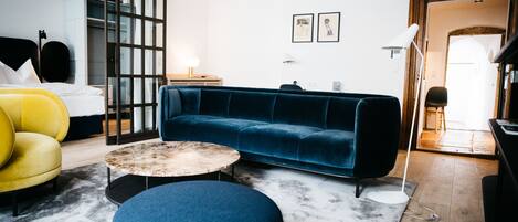 Una sala de estar moderna con un sofá azul, un sillón amarillo, una mesa de centro redonda y un otomano grande.