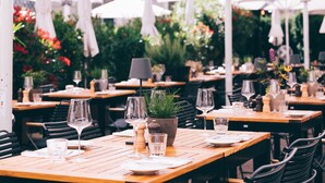 Un restaurante al aire libre con mesas de madera, sombrillas blancas y plantas en macetas.
