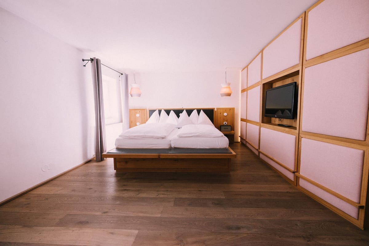Un dormitorio con cama de madera, televisor en la pared y ventana con cortinas.