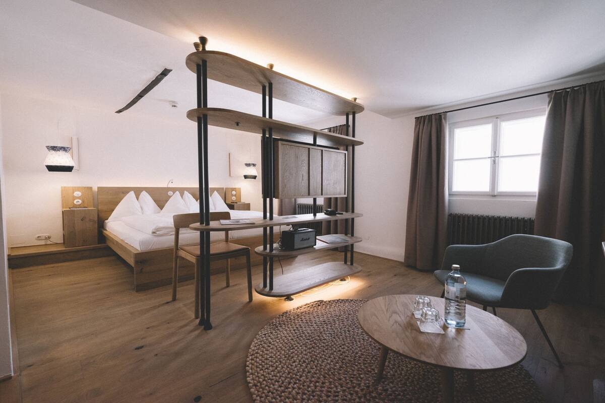 Habitación de hotel con cama, escritorio, silla, mesa redonda y ventana con cortinas.