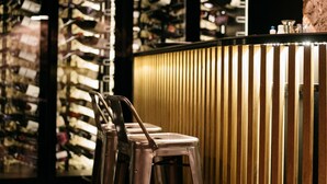Una zona de bar con taburetes metálicos, una barra de madera y copas de vino colgantes.