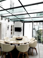 A modern dining area with a glass ceiling, white walls, and a round table surrounded by chairs.