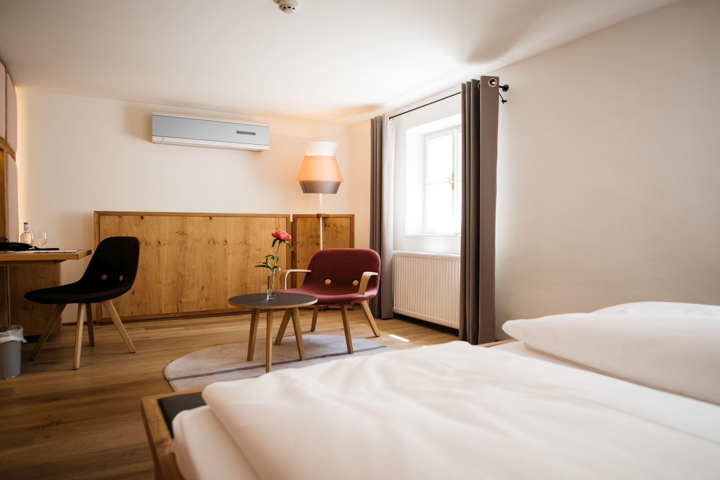 Ein Hotelzimmer mit einem Bett, einem Schreibtisch, zwei Stühlen, einer Lampe und einem Fenster.