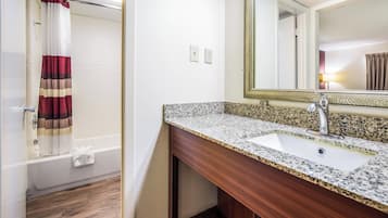 Een badkamer met een bad, een wastafel met een granieten aanrechtblad, en een spiegel met een decoratieve lijst.