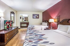 Habitación de hotel con una cama grande, cómoda, televisor, espejo, mesita de noche con lámpara y un cuadro en la pared.
