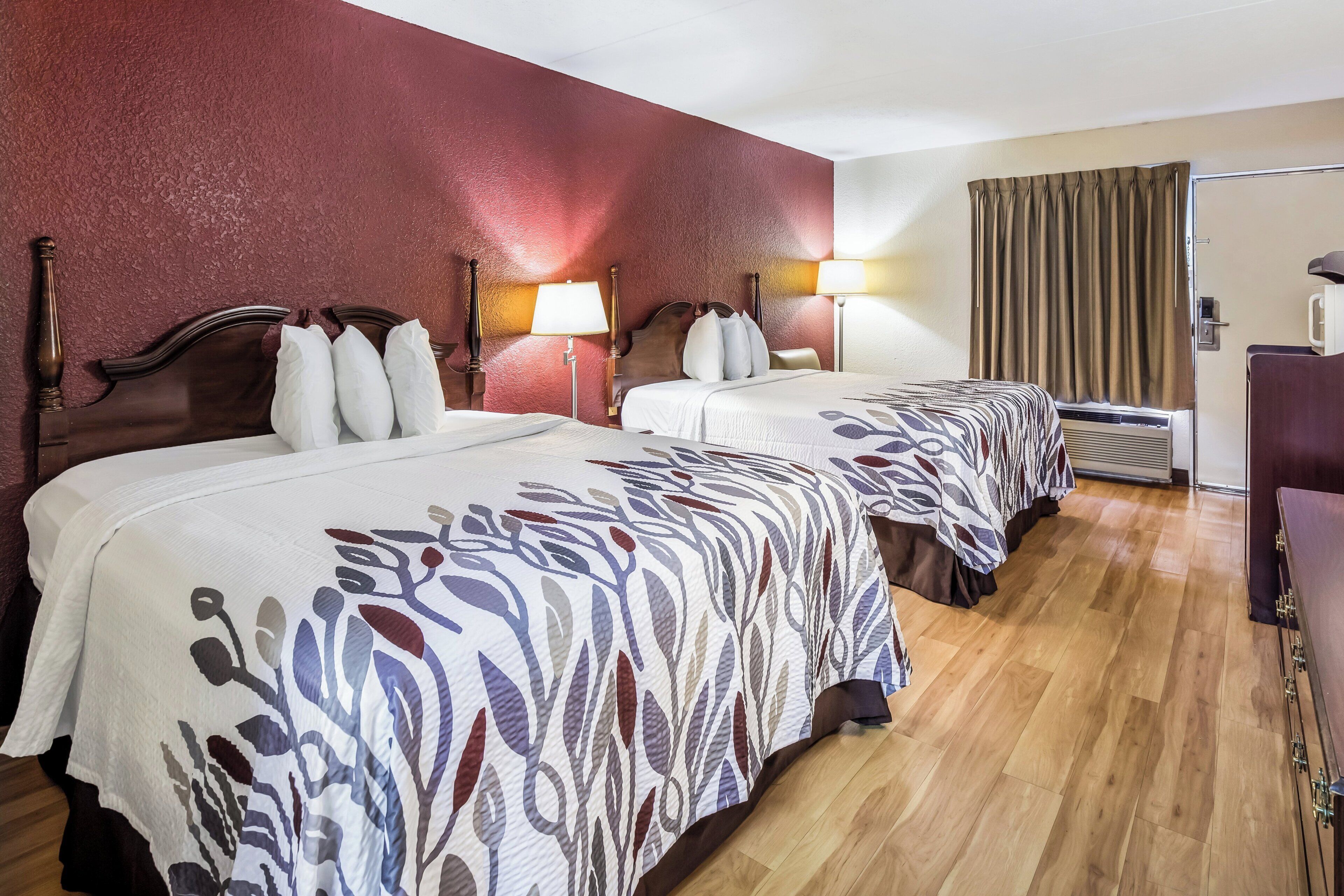 A hotel room with two beds, wooden headboards, and a red accent wall.