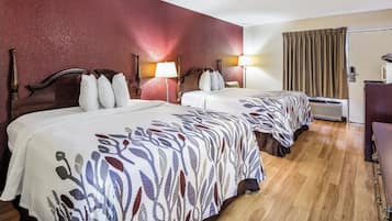 A hotel room with two beds, wooden headboards, and a red accent wall.