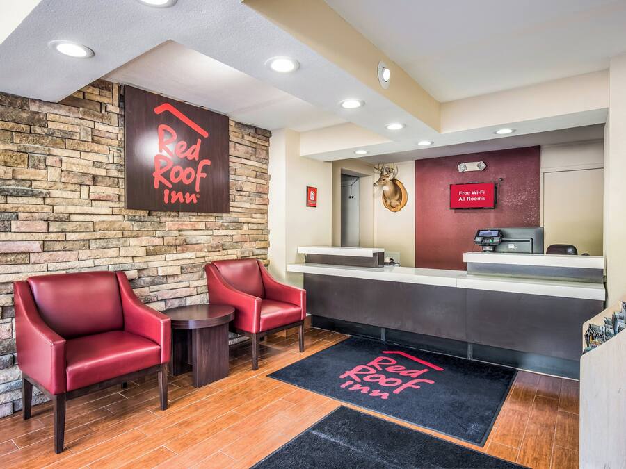 A Red Roof Inn reception area with a stone wall, two leather chairs, a reception desk, and a mounted deer head.