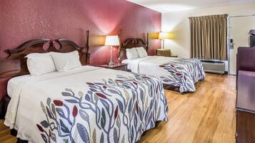 Een hotelkamer met twee bedden, een houten vloer, een rode accentmuur en een raam met gordijnen.