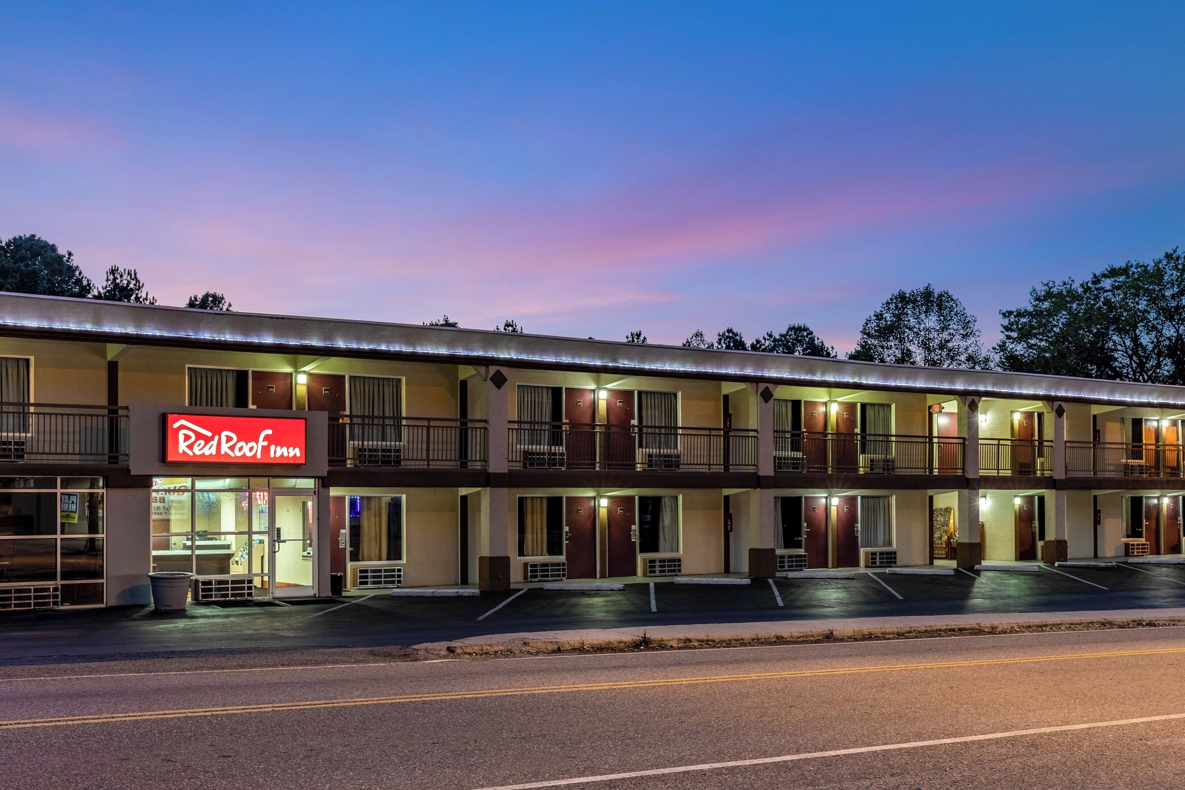 Un motel avec une enseigne rouge, de nombreux balcons et un parking.