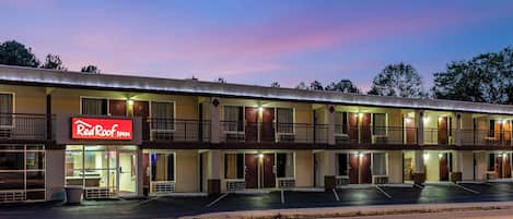 Un motel con un letrero rojo, varias balconadas y un estacionamiento.