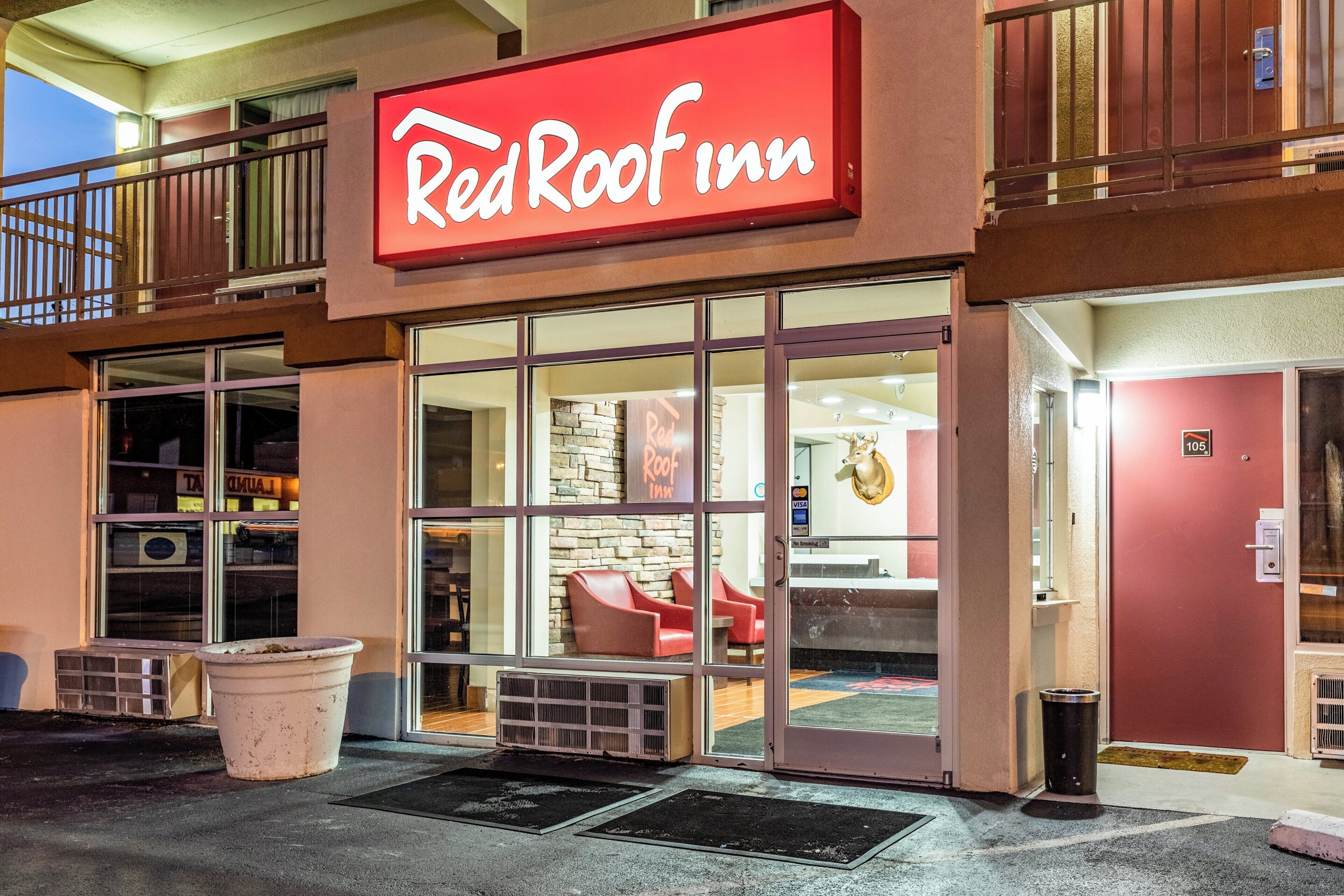 Un hotel Red Roof Inn con un amplio acceso de vidrio, un interior visible con una pared de piedra y una estatua de vaca, y un balcón con barandilla.