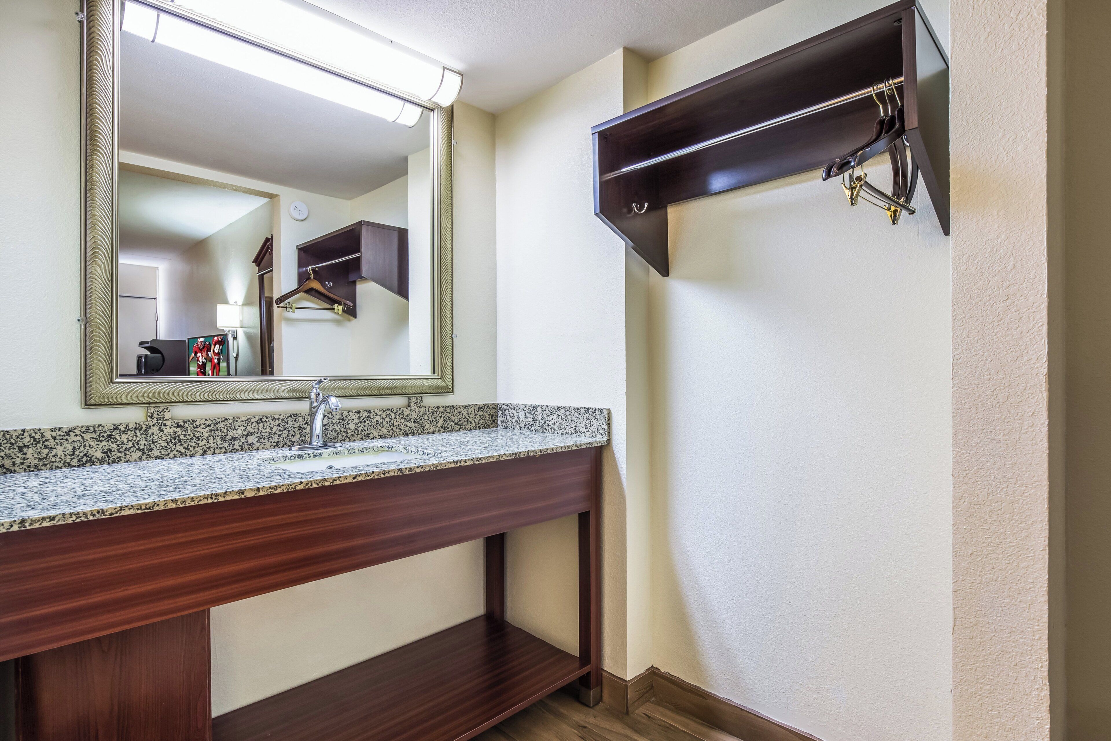 A bathroom with a granite countertop sink, a large mirror, and a dark wooden shelf.