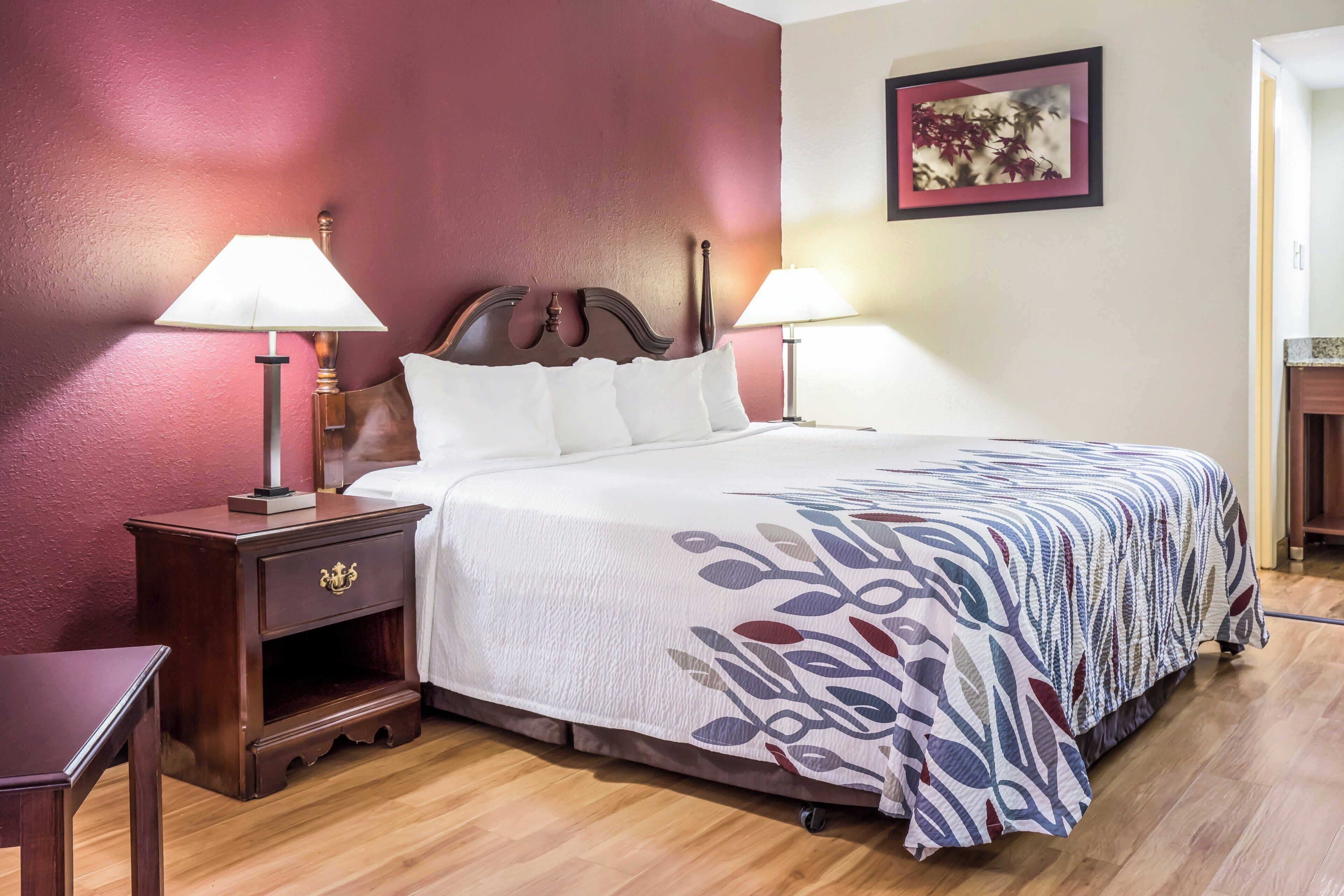 Una camera d'albergo con un letto, due comodini con lampade, un tavolino e un quadro appeso al muro.