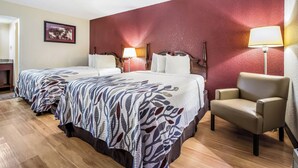 Habitación de hotel con dos camas, una silla, pared roja y un cuadro enmarcado.